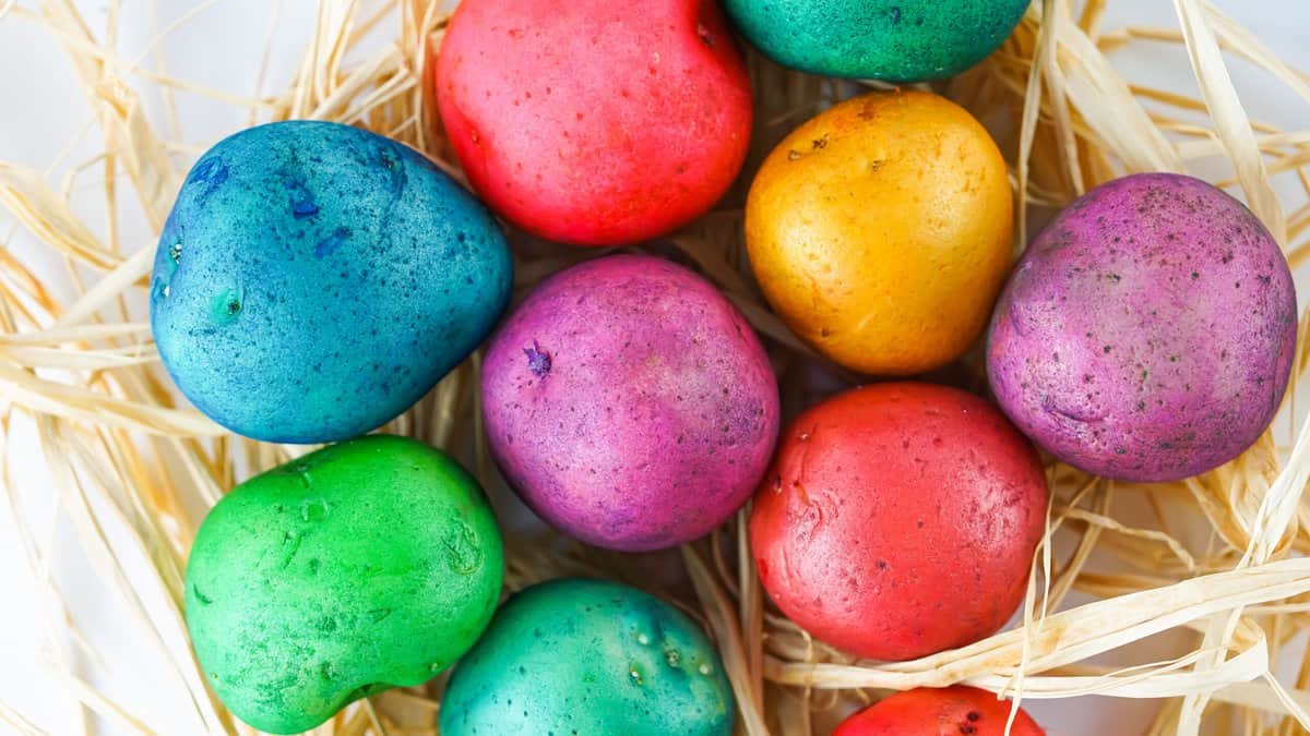 Vibrant tie-dye colored potatoes arranged in a basket on a wooden table. Each potato has a different color pattern and brings a pop of color to the room. Perfect for an Easter decoration or as a fun DIY craft.