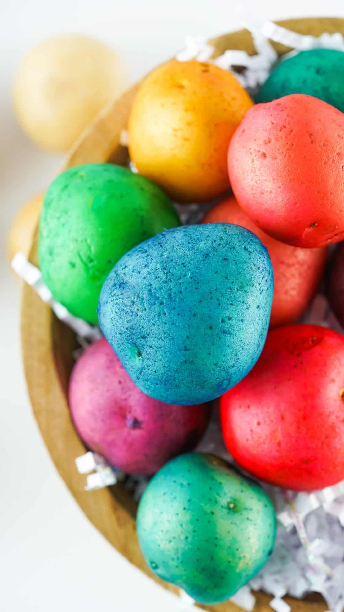 Vibrant tie-dye colored potatoes for potato Easter egg dying arranged in a basket on a wooden table. Each potato has a different color pattern and brings a pop of color to the room. Perfect for an Easter decoration or as a fun DIY craft.