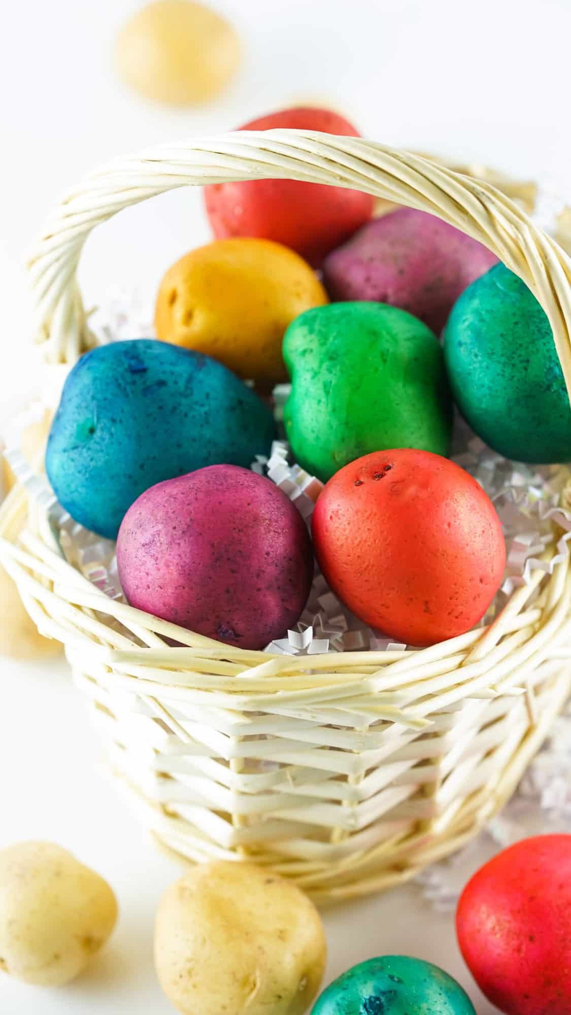 Vibrant tie-dye colored potatoes arranged in a basket on a wooden table. Each potato has a different color pattern and brings a pop of color to the room. Perfect for an Easter decoration or as a fun DIY craft.