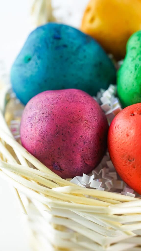 Vibrant tie-dye colored potatoes arranged in a basket on a wooden table. Each potato has a different color pattern and brings a pop of color to the room. Perfect for an Easter decoration or as a fun DIY craft.