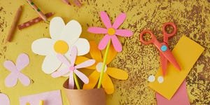 paper flowers made from bright pastels on a yellow background arranged in a brown paper cone with a tag that says mom