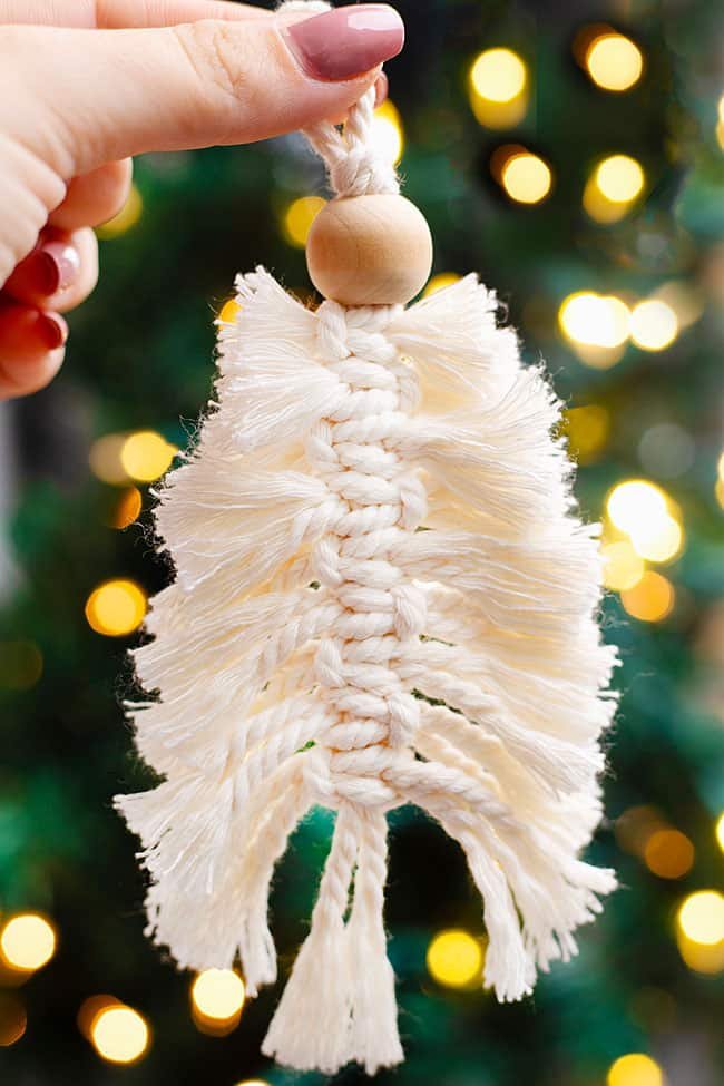 Holding a macrame Christmas tree ornament in front of the Christmas tree