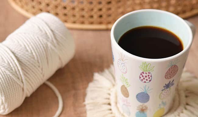 How to Make Macrame Coasters (Easy DIY Tutorial) Macrame coasters with cord and a coffee mug in the background