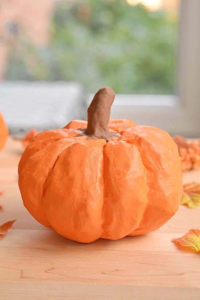 Paper mache pumpkin on wood with fall leaves around it