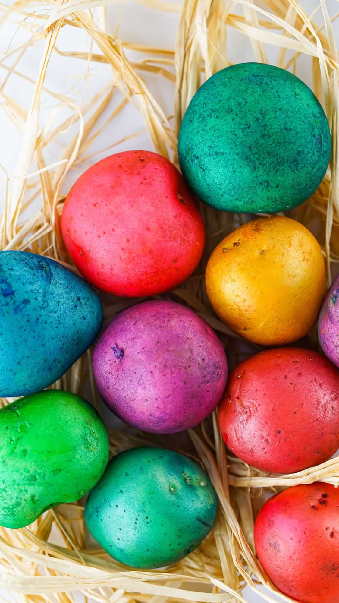 Vibrant tie-dye colored potatoes arranged in a basket on a wooden table. Each potato has a different color pattern and brings a pop of color to the room. Perfect for an Easter decoration or as a fun DIY craft.