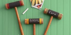 three croquet mallets turned into garden markers for a summer craft project with the words corn and basil written in chalk on the heads