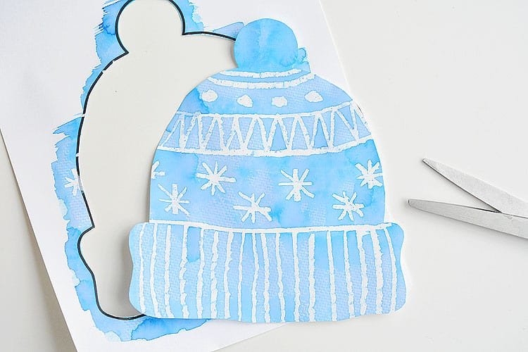 This winter hat art project for kids is such a fun winter craft idea! Use the free printable winter hat template to have a fun day of crafting at home or in the classroom! This process art idea lets you experiment with creating texture in watercolor and shows the magic of painting over crayon with watercolour paint! There's even instructions for making a DIY yarn pom pom!