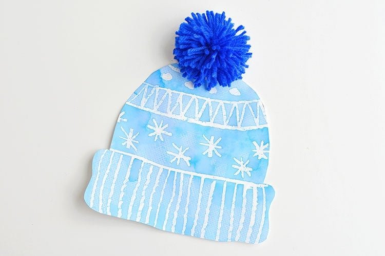 This winter hat art project for kids is such a fun winter craft idea! Use the free printable winter hat template to have a fun day of crafting at home or in the classroom! This process art idea lets you experiment with creating texture in watercolor and shows the magic of painting over crayon with watercolour paint! There's even instructions for making a DIY yarn pom pom!