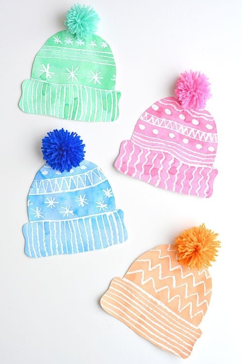 This winter hat art project for kids is such a fun winter craft idea! Use the free printable winter hat template to have a fun day of crafting at home or in the classroom! This process art idea lets you experiment with creating texture in watercolor and shows the magic of painting over crayon with watercolour paint! There's even instructions for making a DIY yarn pom pom!