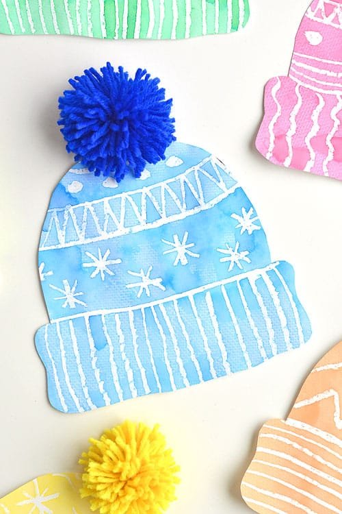 This winter hat art project for kids is such a fun winter craft idea! Use the free printable winter hat template to have a fun day of crafting at home or in the classroom! This process art idea lets you experiment with creating texture in watercolor and shows the magic of painting over crayon with watercolour paint! There's even instructions for making a DIY yarn pom pom!