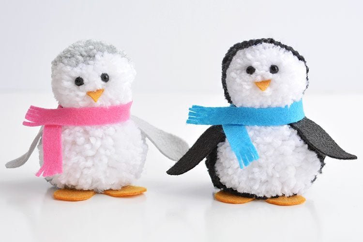 Grey and white pom pom penguin standing beside a black and white penguin