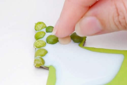 Close-up of fingers pressing lentils into white glue on green tree shape