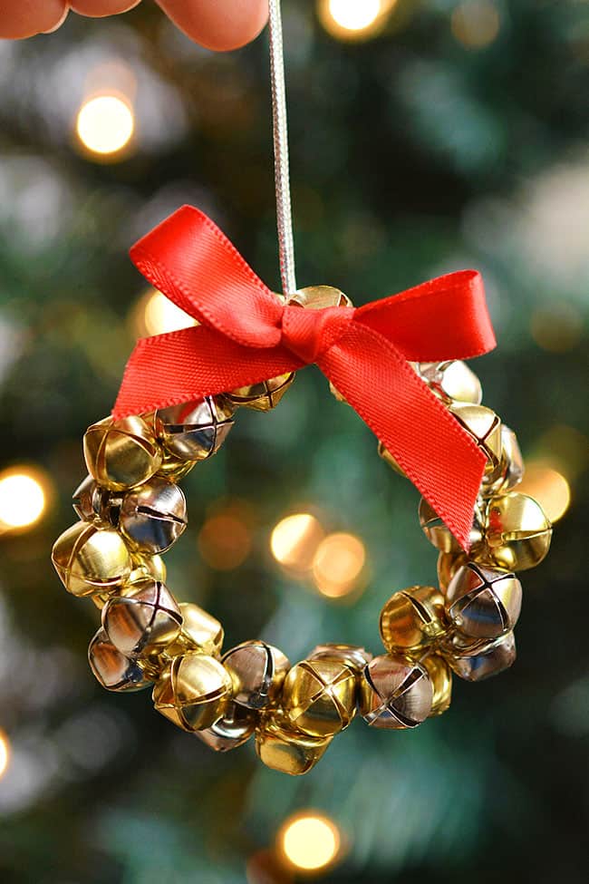 Jingle bell ornament held in front of a lit Christmas tree