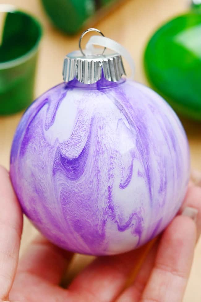 Holding a purple and white marbled paint pour Christmas ornament ball