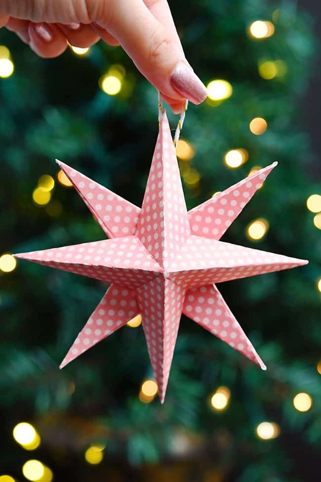 Holding a paper star ornament in front of a lit Christmas tree