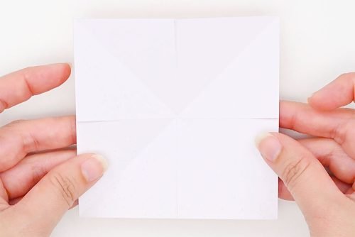 Hands holding a square piece of paper showing small cuts along 4 creases