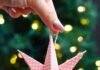 How to Make Paper Star Ornaments Holding a paper star ornament in front of a lit Christmas tree