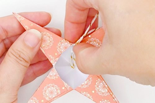 Fingers pressing craft twine into hot glue on paper star