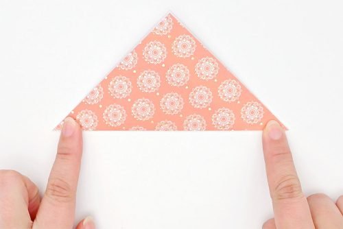 Decorative paper folded into a triangle with a finger holding down each corner