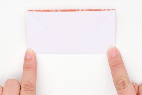 Square paper folded in half with a finger holding down each bottom corner