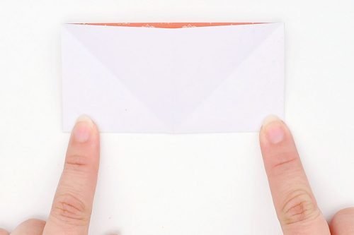 Square paper folded in half with a finger holding down each bottom corner