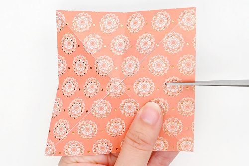 Scissors cutting along a fold on one side of square piece of decorative paper