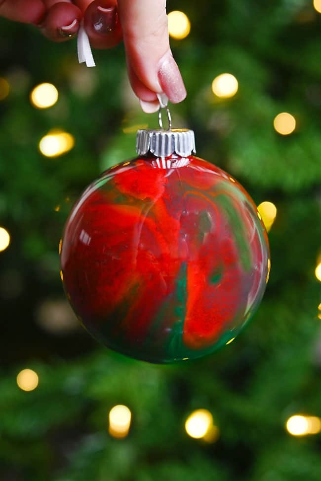 Holding a pour paint ornament in front of a lit Christmas tree