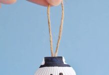How to Make Seashell Snowman Ornaments Seashell snowman ornament hanging in front of a blue background