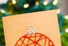 How to Make String Art Christmas Cards String art Christmas card held in front of a Christmas tree